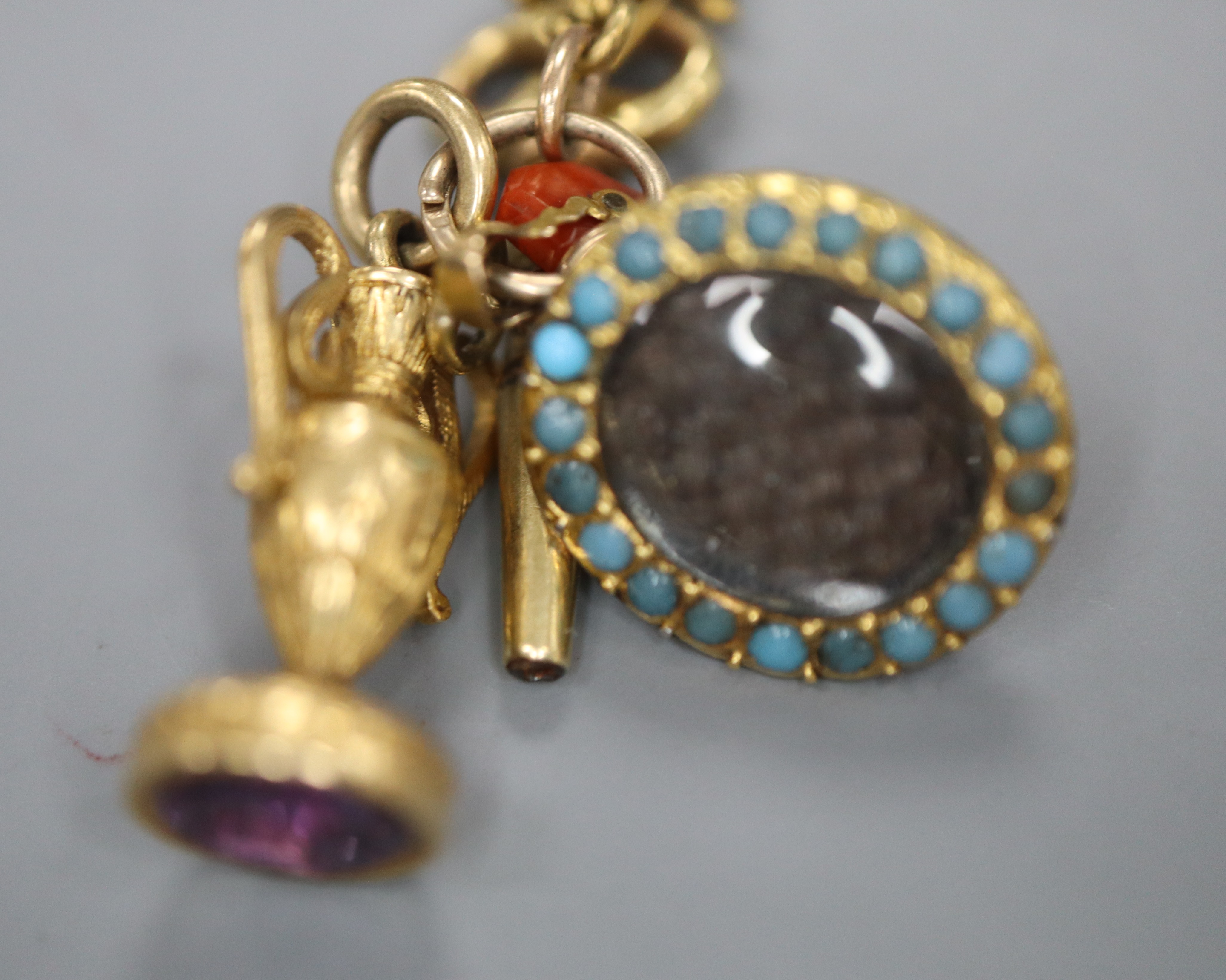 A group of four assorted charms on a yellow metal small chain, including a watch key and carnelian seal.